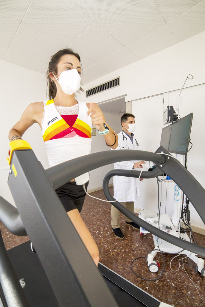 Deportista con electrodos corriendo en cinta rodante mientras el médico monitoriza la prueba